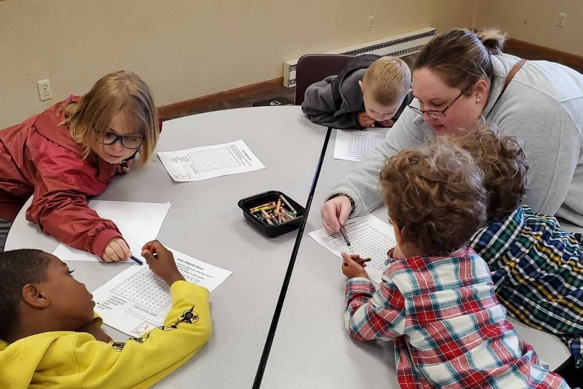 Adult helping National Home resident children at a table as they fill out papers.